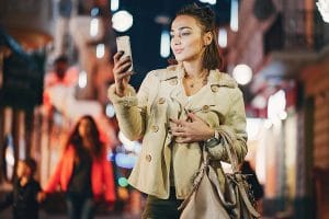 Young fashionable Russian woman walking using her smartphone while walking on the street in the evening