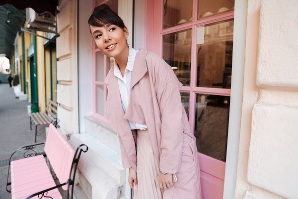 Smiling pretty Russian girl in a pink coat standing outside her favorite café looking sideways