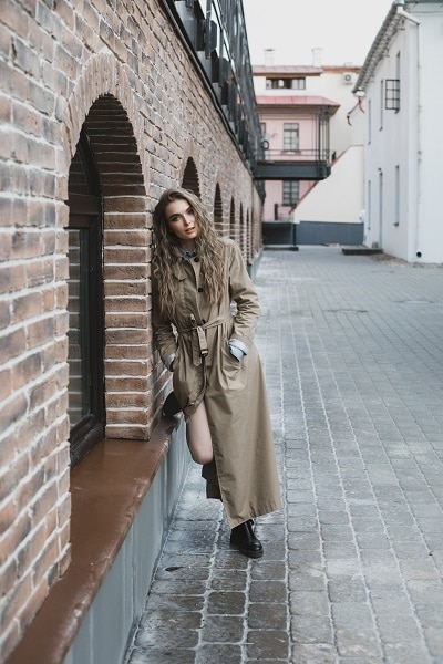 Pretty serious Russian woman standing nearby a brick wall with her hands in the pockets